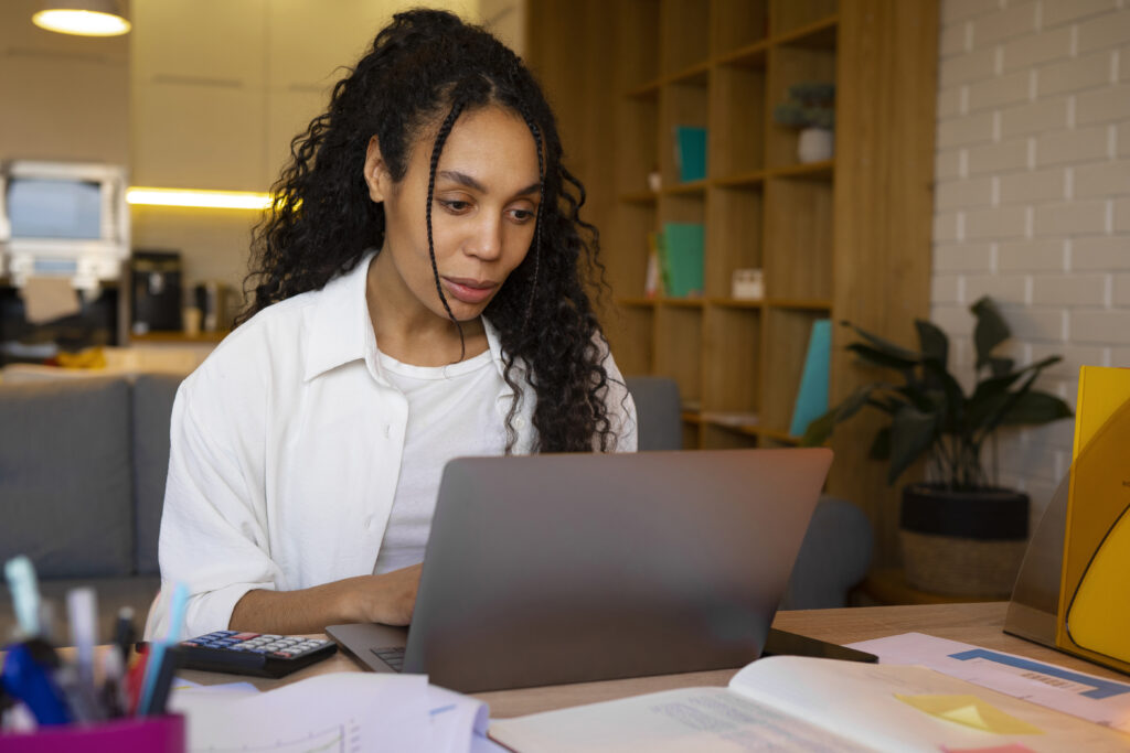 Mulher estudando em um notebook, com materiais de apoio ao redor, representando foco e educação em ambiente digital.